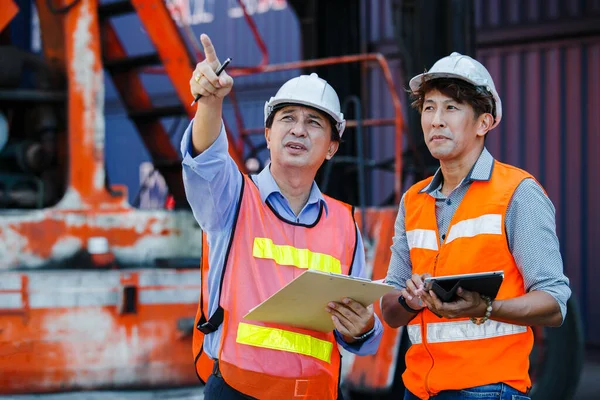 stock image Teamwork engineer foreman, Asian foreman holding clipboard and tablet control loading cargo ship import export, Container terminal cargo. Officers working in container import company.