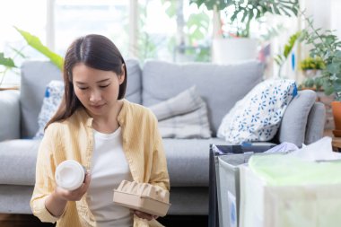 Asyalı genç bir kadın evde oturuyor kağıt ve plastik atıkları ayırıyor. Geri dönüşüm için çöp ayıklama. Küresel ısınmanın azaltılması