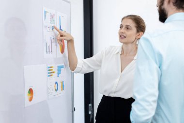 Kadın yönetici parmak grafiğini gösteriyor ve toplantı odasındaki sunumlara bakıyor. İş adamları, şirkete yatırımlarını sunarlar. İş projesi planlama hedefi.