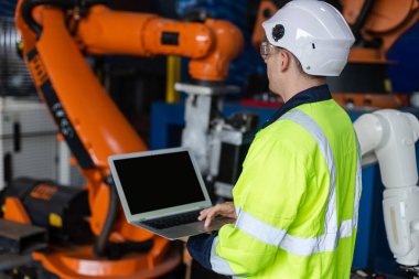 Erkek mühendis dizüstü bilgisayarı kullanıyor ve robot kolu otomatik kontrol ediyor. Endüstriyel üretim sırasında robot otomasyonu. Fabrikada robotik test performansı.
