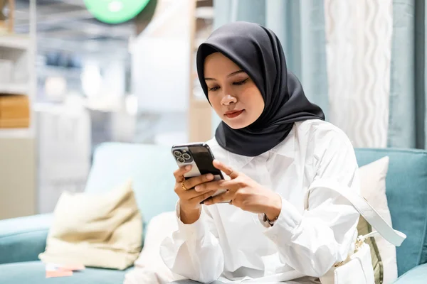 快乐的穆斯林女性头戴头巾 坐在家里沙发上用智能手机的肖像 聊天在网上传递信息 用手机购物 — 图库照片