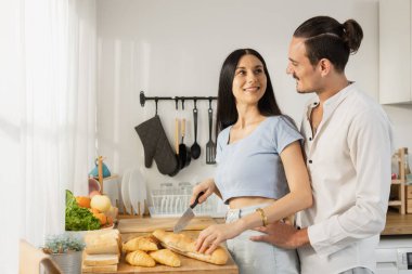 Mutlu beyaz çift, mutfakta kahvaltı hazırlarken iyi eğlenceler. Birlikte aşk. Karı koca ekmek kesmeyi kucaklıyor, yemek yapmayı seviyor. Erkek ve kadın neşeli romantik ilişki.