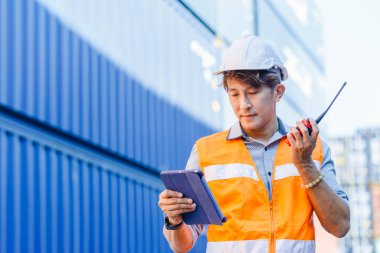 Foreman radyo telsizi kullanıyor ve ithalat için kargodaki tablet kontrol kutuları kullanıyor. Profesyonel mühendis konteynır kutusunu kontrol ediyor..