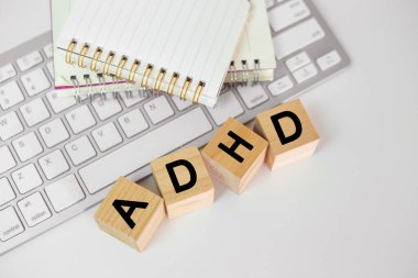 Tahta küp bloktaki ADHD 'nin kısaltması bilgisayar klavyesi ve beyaz masadaki not defteri. Dikkat eksikliği Hiperaktivite Bozukluğu. ADHD konsepti.