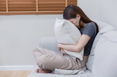 Yatak odasında yalnız başına depresyonda olan bir kadın. Kadın baş ağrısı, mutsuz duygu. Kanepede tek başına oturmak. Depresyondaki kadın yastığı kucaklıyor. Zihinsel sağlık sorunları umutsuzluğa kapıldı.