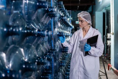 Elinde pano tutan kadın işçiler, tüketicilere vermek üzere plastik şişelere su doldurmadan önce büyük içme suyu tanklarının kalitesini kontrol ediyorlar. Fabrika üretim hattında su şişeleri. 