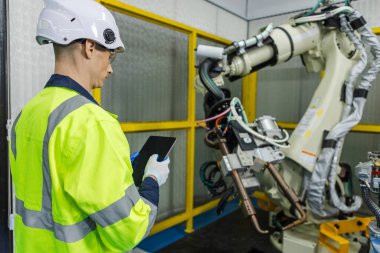 Endüstriyel modern fabrikada otomasyon robotları kullanan teknisyen adam. Otomasyon robotunu fabrikada kontrol eden erkek işçi.