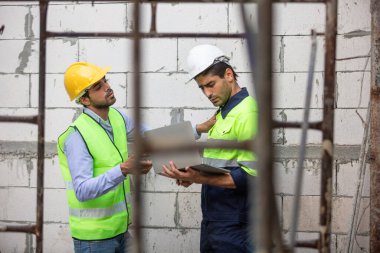 Ekip mühendisi dizüstü bilgisayarı kullanarak bina inşaatı yapıyor. Erkek mimar ev inşaatında kalite teftiş yapısını ayakta tutuyor. Ustabaşı iş yerinde.