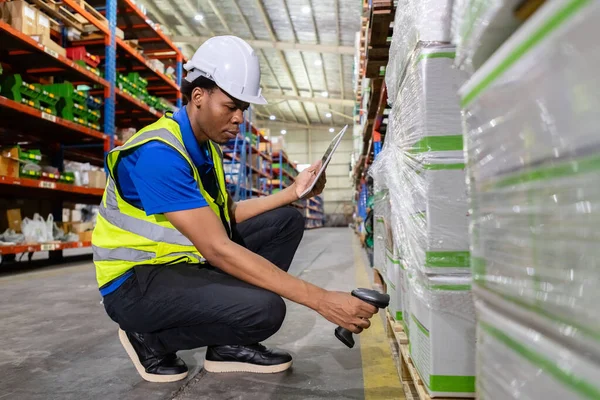 男性のアフリカの工場会社従業員のスキャン ボックスは倉庫のタブレットが付いている商品の棚のプロダクトの数を点検します ロジスティクスと流通で働く人間 輸出入倉庫について ストックフォト