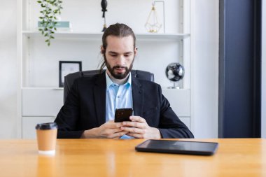 Akıllı telefon kullanan, sakallı, beyaz, yakışıklı bir iş adamı. Kişisel mobil iletişim. Adam mesaj gönderir ya da arama bilgisini arar. Çalışma çevrimiçi sistem üzerinden sipariş ediliyor.