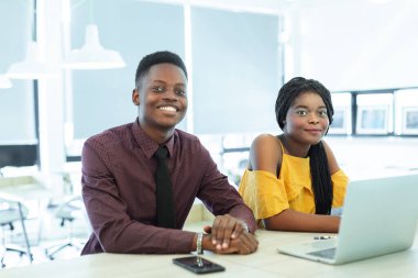 Kadın ve erkek, Afro-Amerikan siyah tenli, ofis masasında oturan kameraya bakıyor. İş adamı takımı başarılı oldu..