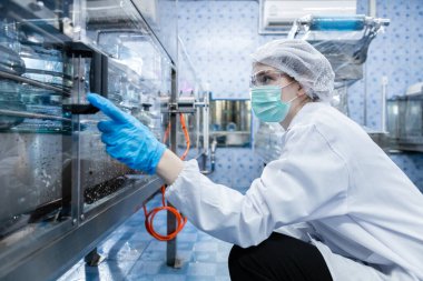 Kadın işçi, suyu plastik şişelere doldurup tüketicilere götürmeden önce kaliteli içme suyunu kontrol ediyor. Fabrika üretim hattında su şişeleri.