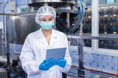 Tablet üzerinde bilgi arayan kadın işçiler fabrika üretim hattında kaliteli içme suyunu kontrol ediyorlar.