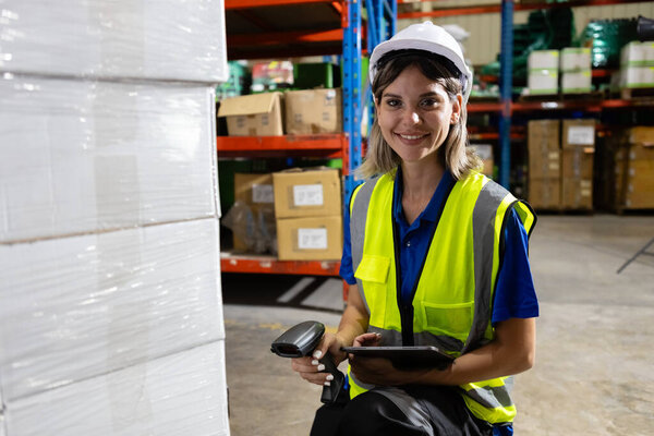 Женщина-блондинка волосатого завода компании сотрудник сканирования коробки проверки количества продуктов на полках товаров с планшетом на складе. Женщина улыбается, глядя на камеру, работающую в логистике и дистрибуции.