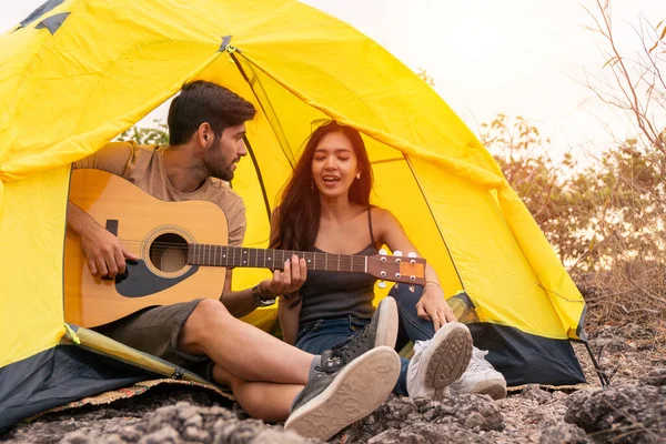 Couple romantic camping on mountain sitting in tent with playing guitar singing relaxing lifestyle vacation evening time, camping travel concept.