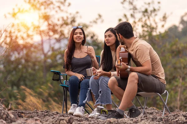 Erkek ve iki kadın birlikte mutlu, ormanda piknik, dağda kamp. Gitar çalmak, şarkı söylemek, hayat tarzı dinlenmek, akşam tatilleri, kamp yapmak, seyahat kavramları..