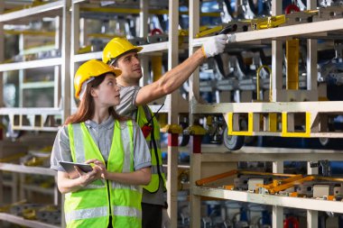 Erkek ve kadın tablet kullanıyor ve depodaki raflardaki denetleme malları otomobil parçalarını tararken barkod okuyucu kullanıyor. Lojistik ithalat otomobil parçaları. Depolama listesindeki stok ürünü.