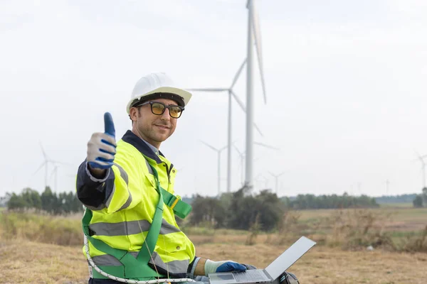 Wind turbine technician checking and maintenance at turbine station. Man engineer thumb up working at energy wind generator. clean energy source.