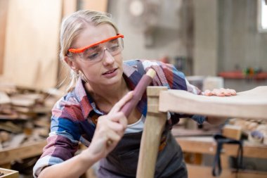 Genç marangoz kadın ahşap cilalama için zımpara kağıdı kullanıyor. Fabrika endüstrisi ahşap mobilya. Profesyonel tamirci..