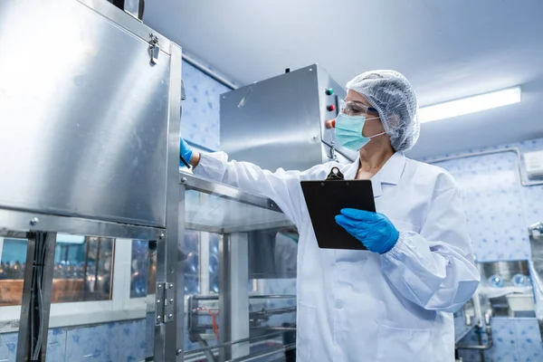 Female worker using tablet checking quality drinking water before process of filling water into plastic bottles to bring out to consumers. Water bottles on production line of factory.