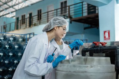 Kadın işçi, temiz içme suyunu filtreleme sürecini kontrol ediyor. Şişelere su doldurma işleminden önce yönetim sistemi. Fabrikanın su üretim hattı.