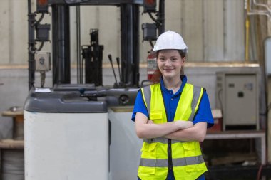 Kafkasyalı kadın mühendisin portresi, fabrika endüstrisinde forklift ile yan yana duran beyaz kasklı, gülümseyen kollar takıyor. Kadın işçi forklift depoda lojistik ithalat-ihracat yapıyor..