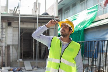 İnşaat mühendisi. İnşaat alanında duran mutlu mühendis üniforması giyiyor. İnşaat teftişini işçiler denetliyor.