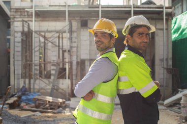 İnşaat mühendisi ekibi. İnşaat alanında kesişen iki adam kameraya bakarken üniforma giyiyor. İnşaat teftişini işçiler denetliyor.