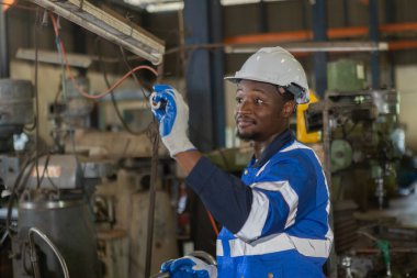 Üniforma giyen ve şapka takan erkek Afro-Amerikan işçiler fabrika endüstrisinde demir kesme makinesinde çalışıyorlar. Mühendislik işçisi iş makinası torna. Ağır sanayi konsepti.