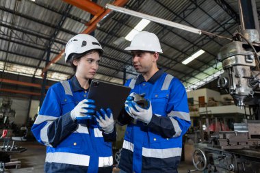 Üniformalı güvenlik kaskı takan takım çalışanları fabrika endüstrisinde çalışan tablet kullanıyorlar. Erkek ve kadın işçi makine torna metali. Ağır sanayi konsepti.