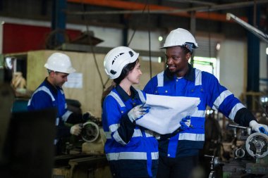 Üniforma giyen takım çalışanı güvenlik beyin fırtınası yapıyor. Planı tutuyor. Çalışma yönetimi fabrikada çalışıyor. Mühendislik endüstrisi metal ürünleri mekanik üretiminde çalışıyor.