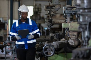 Üniformalı güvenlik şapkası takan erkek Afro-Amerikan işçiler fabrika endüstrisinde çalışan bir tablet kullanıyorlar. Mühendislik işçisi iş makinası torna. Ağır sanayi konsepti.