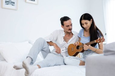 Yatak odasında ukulele oynayan mutlu çift. Müzikten hoşlanan erkek ve kadın ailede mutlu aktiviteler yaratır. Genç çift enstrümanla mutlu ve romantik.