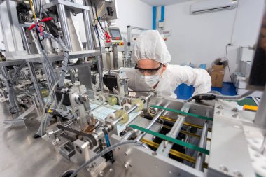 Makine personeli, maske üretim departmanı. Koruyucu giysi giyen mühendis, maske kalitesini ölçüyor. makine üretim fabrikası.