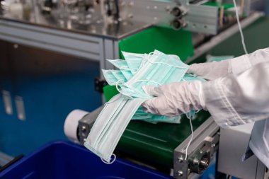 Üretici fabrikasının kaliteli tıbbi maskesini kontrol eden bir kadın işçi. Yüz maskesi fabrikası. Üretici tıbbi ekipman.