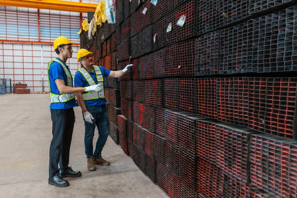 Worker wearing safety uniform using digital tablet inspect product iron metal on shelves in warehouse. Two man engineer worker check stock stainless inspecting in storage logistic factory.