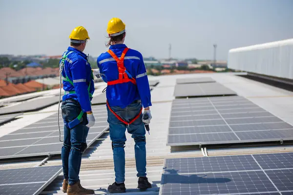 Teknisyenler endüstriyel bir fabrikanın çatısındaki güneş panellerinin standartlarını inceliyorlar. Doğadan elde edilen elektrik enerjisi güneş ışığı temiz yenilenebilir enerji.