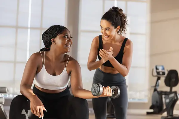 Latina female coach training women African American plus-size holding dumbbells lifts weights exercise in gym. sport training weights fitness, Exercise to lose weight, take care of health.