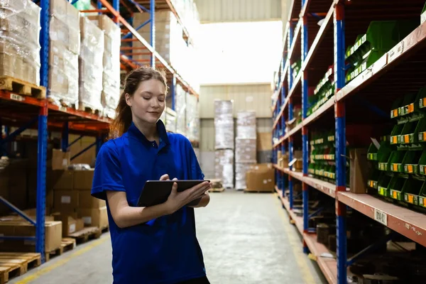 Female worker wearing safety uniform and hard hat using tablet checking inspect goods on shelves in warehouse. women worker check stock inspecting product in factory.