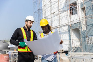 İnşaat mühendisi ve kadın Afro-Amerikan inşaat alanındaki iş kalitesini kontrol ediyor. Altyapı inşaatında çalışan çeşitli uluslardan oluşan bir ekip..