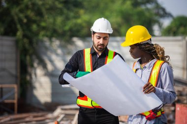 İnşaat mühendisi ve kadın Afro-Amerikan inşaat alanındaki iş kalitesini kontrol ediyor. Altyapı inşaatında çalışan çeşitli uluslardan oluşan bir ekip..