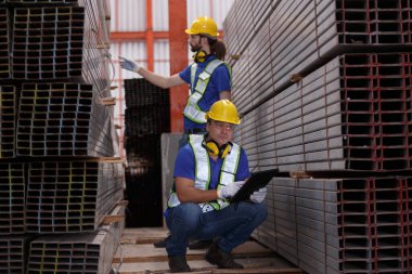 Dijital tablet kullanarak güvenlik üniforması giyen işçiler depodaki raflarda demir metali inceliyor. İki adam mühendis stok paslanmaz kontrol depolama lojistik fabrikası.