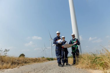 Ekip mühendisi rüzgar türbini işçi üniforması güvenlik anketi operasyon planlama yel değirmeni temiz enerjisini tartışıyor. Alternatif teknoloji çevreyi korur küresel ısınma sorunlarını azaltır.