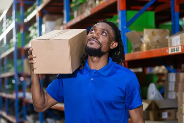 Man american african professional worker wearing safety uniform and hard hat holding box product on shelves in warehouse. Man worker check stock inspecting in storage logistic factory.
