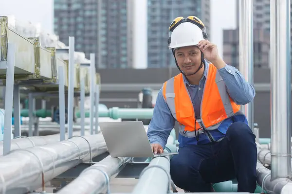 Man Industrial engineer using laptop working at rooftop construction. Male technician working checking HVAC system building factory. Installing large air conditioning system.