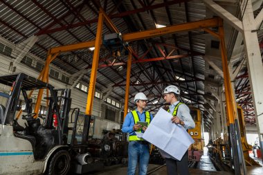 Tren yolu teknisyeni üniformalı güvenlik kaskı takıyor. Tablet ve taslak kontrol planı demiryolu istasyonunda duruyor. Fabrikada lokomotif tamircisi.