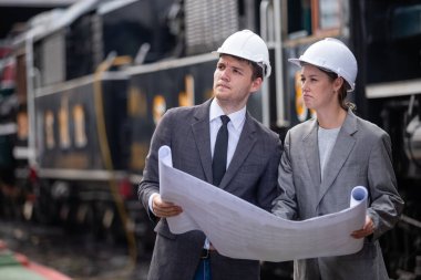 Güvenlik kaskı takan mimar ve mühendisler demiryolu tasarımı taslağı okuyorlar. Tren bakım bölümü fabrikasının teftiş istasyonu..