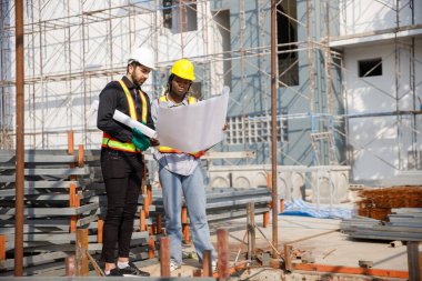 İnşaat mühendisi ve kadın Afro-Amerikan inşaat alanındaki iş kalitesini kontrol ediyor. Altyapı inşaatında çalışan çeşitli uluslardan oluşan bir ekip..
