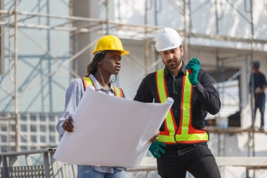 İnşaat mühendisi ve kadın Afro-Amerikan inşaat alanındaki iş kalitesini kontrol ediyor. Altyapı inşaatında çalışan çeşitli uluslardan oluşan bir ekip..