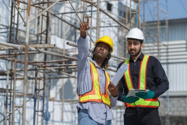 İnşaat mühendisi ve kadın Afro-Amerikan inşaat alanındaki iş kalitesini kontrol ediyor. Altyapı inşaatında çalışan çeşitli uluslardan oluşan bir ekip..
